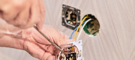 Hands of an electrician installing an electrical outlet in a new house. Assembly of the electrical network in the room, installation of the electrical network